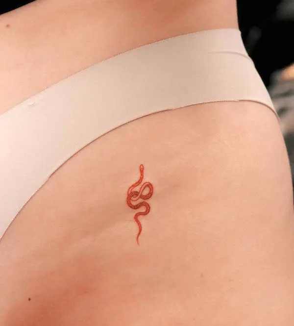 Tiny red snake hip tattoo by @nhi.ink